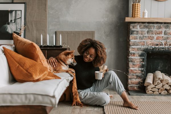 Ist auf dem Boden sitzen gesund? Frau sitzt auf dem Boden vor ihrem Hund auf dem Sofa. Der Link führt zu einem Blogbeitrag zum Thema "Auf dem Boden sitzen"