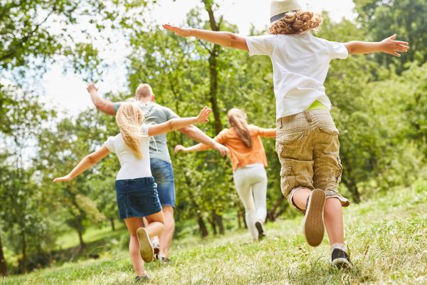 Bewegung ist auch für Kinder ein wichtiges Element. Mann, Frau und zwei Kinder bewegen sich im freien, sie strecken arme weit aus und sind alle von hinten zu sehen.