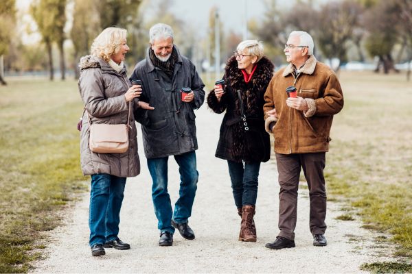 Mehr Bewegung im Alltag. Vier ältere Menschen gehen gemeinsam auf einem Weg im Park und unterhalten sich beim Spazierengehen.
