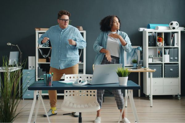 Bewegungspausen für Erwachsene. Zwei Personen bewegen sich im Büro neben einem Schreibtisch und machen eine aktive Pause während der Arbeit.