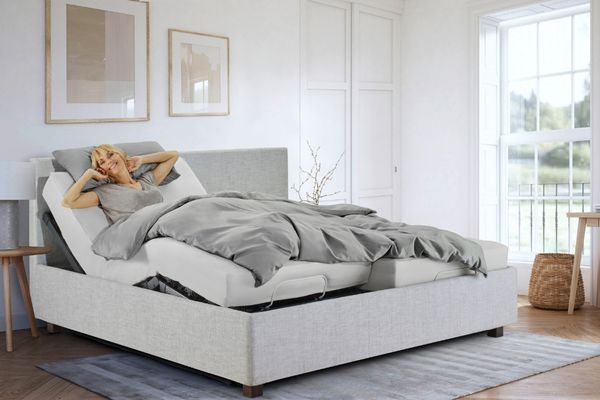 Die Basis für erholsamen Schlaf und einen gesunden Rücken ist ein ergonomisches Bettsystem. Der Link führt zu einer Übersichtsseite zu rückenfreundlichen Bettsystemen. Das Bild zeigt eine lächelnde Frau in einem Bett.